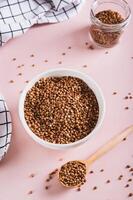 White bowl with raw whole grain buckwheat on pink background vertical view photo