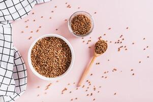 Raw buckwheat in a bowl and wooden spoon on a pink background top view photo