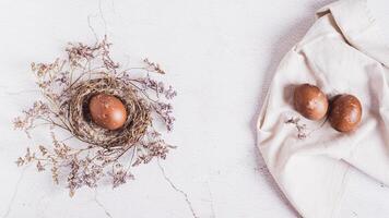 Homemade naturally colored eggs in a nest and on a cloth on a table top view web banner photo