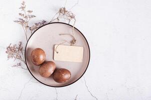 Homemade natural painted eggs for Easter and card on a plate, cloth and dried flowers top view photo