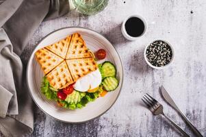 Waffle bread sandwich with poached egg and vegetables on a plate on the table top view photo