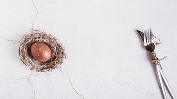 Homemade naturally colored egg in a nest and cutlery for Easter on the table top view web banner photo