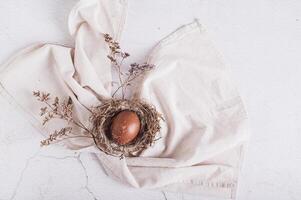 Homemade naturally colored egg in a nest on a napkin and dried flowers on the table top view photo
