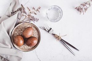 Naturally colored eggs for Easter on a plate, cutlery and a glass of water on the table top view photo