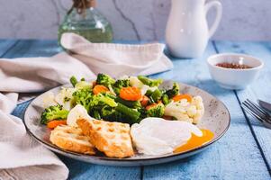 Mix of boiled vegetables, poached egg and waffle toast on a plate on the table photo