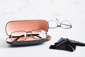 Eyeglasses in an open hard case and a cleaning cloth in front of other glasses on a table photo