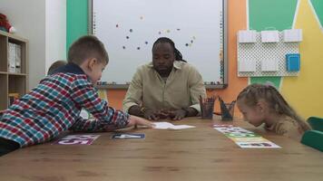 afrikansk amerikan lärare och en grupp av barn är inlärning tal medan Sammanträde på de tabell i de klassrum.skola för barn, undervisning tonåringar, få kunskap, lära sig de språk. video