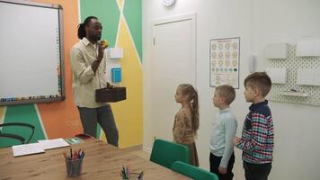 un africain américain prof et une groupe de les enfants sont en train d'étudier des fruits et animaux dans le salle de classe.école pour enfants, enseignement adolescents, Gain connaissance, apprendre le langue. video