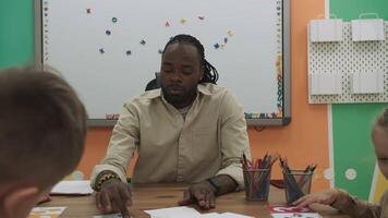 African American teacher and a group of children are learning numbers while sitting at the table in the classroom.School for Children, Teaching Adolescents, Gain Knowledge, Learn the Language. video