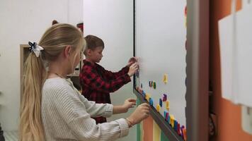 Kinder Schüler lernen Englisch durch Herstellung Wörter von Briefe auf ein magnetisch Tafel. Schule zum Kinder, Lehren Jugendliche, dazugewinnen Wissen, lernen das Sprache. video