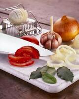 tomato being cut on kitchen board with garlic onion and egg photo