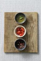 wooden board with mini bowls with tomatoes, pepper and olive oil photo