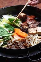 paso a paso guía a Sukiyaki, un clásico japonés plato con verduras, manteca, salsa, carne y tofu queso foto