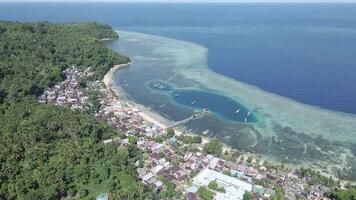 aéreo Visão do motor barcos ancorado em corre ilha com palafita casas às a costas em de madeira área coberta. brilhante azul céu.. maluku, Indonésia, abril 18, 2024 video