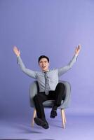 Portrait of Asian business man sitting on sofa, isolated on purple background photo