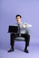 Portrait of Asian business man sitting on sofa, isolated on purple background photo