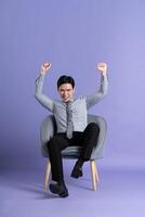 Portrait of Asian business man sitting on sofa, isolated on purple background photo