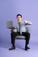 Portrait of Asian business man sitting on sofa, isolated on purple background photo