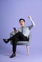 Portrait of Asian business man sitting on sofa, isolated on purple background photo