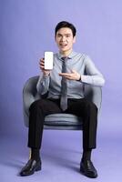 Portrait of Asian business man sitting on sofa, isolated on purple background photo