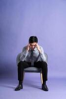 Portrait of Asian business man sitting on sofa, isolated on purple background photo