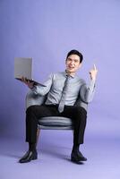 Portrait of Asian business man sitting on sofa, isolated on purple background photo