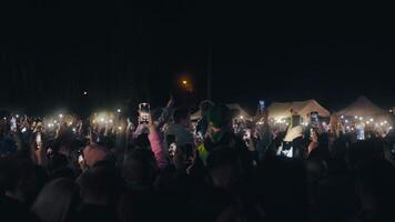 persone su il concerto. folla con luci su il musica mostrare. pubblico fabbricazione fotografie di il gruppo musicale su smartphone nel davanti di il palcoscenico. applauso e cantando folla video