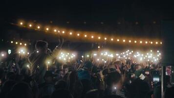 People on the concert. Crowd with lights on the music show. Audience making photos of the band on smartphones in front of the stage. Cheering and singing crowd video