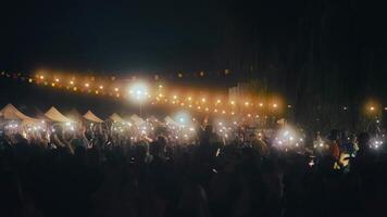 persone su il concerto. folla con luci su il musica mostrare. pubblico fabbricazione fotografie di il gruppo musicale su smartphone nel davanti di il palcoscenico. applauso e cantando folla video