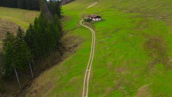 Lonely traditional German house stands on mountain with road leading to it in Bavarian Alps. Single hut for tourists in high mountains with a unpaved road. Aerial view of hills and farmhouse Germany. video