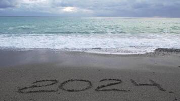 Happy New Year 2025 hand written digit 2024 washed by wave on the sea beach. Abstract background of coming New Year 2025 and leaving year of 2024. video