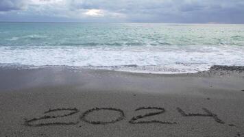 Happy New Year 2025 hand written digit 2024 washed by wave on the sea beach. Abstract background of coming New Year 2025 and leaving year of 2024. video