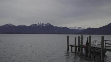 March 15, 2024, Lake Chiemsee, Chiemgau, Bavaria, Germany. Beautiful sunset on Bavarian lake Chiemsee with view of mountains and boat from pier. Chiemgau and Schliersee Alps. Priener Scharen. video