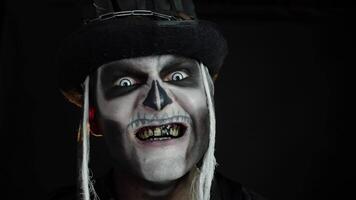 Creepy man face with skeleton makeup in top-hat appearing on black background. Halloween party video