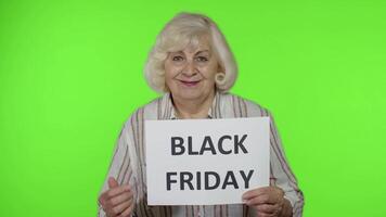 Elderly grandmother holding Black Friday text inscription banner. Senior woman rejoicing discounts video