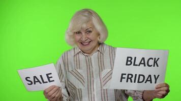 Senior grandmother showing Sale word and Black Friday inscription advertisement banners. Discounts video