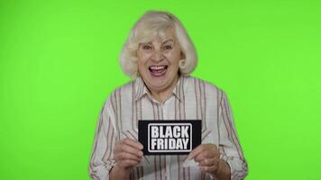 anziano nonna mostrando nero Venerdì iscrizione Nota, sorridente, guardare soddisfatto con Basso prezzi video