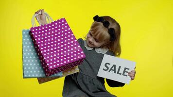 Cute joyful kid girl in shirt showing Sale word advertisement inscription banner and shopping bags video