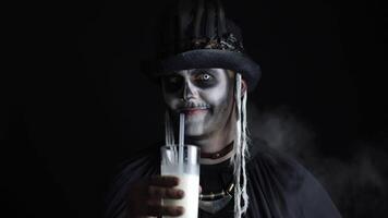 Scary guy in carnival costume of Halloween skeleton looking at camera, drinks milk from a glass video