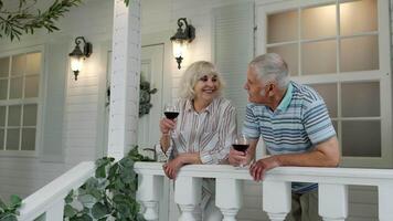 senior ouderen Kaukasisch paar drinken wijn in veranda Bij huis. gelukkig volwassen gepensioneerd familie resting video