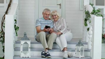 Senior couple using digital tablet in porch at home. Watching funny s on social media network video