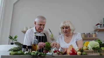 mayor abuelos en cocina. gracioso abuelo bromas en abuela. poniendo un lechuga acerca de su cabeza video