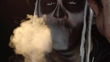 Close-up of sinister man with skull makeup making faces and exhaling cigarette smoke from his mouth video