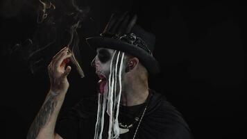 Scary guy in carnival costume of Halloween skeleton smoking cigar, making faces, showing tongue video