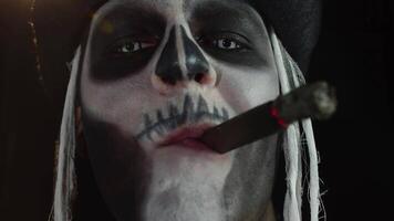 Close up shot of creepy man face with skeleton makeup smoking cigar, making faces, looking at camera video