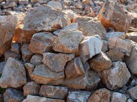 Stone wall of large mountain stones with burrs. A mountain of grey cobbles. Texture. Background. Horizontal photo