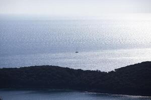 A small sailing ship sailing along the sea surface of the Adriatic Sea. An island with green trees. View from above. Montenegro. Budva. Horizontal. photo