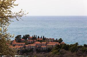 Sveti Stefan Island in the Adriatic Sea, Montenegro. Island with houses and trees. See through the trees from above. Balkans. Background photo