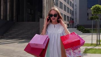Girl walking from shopping mall with shopping bags and talking on mobile phone about purchases video