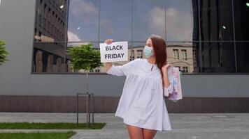 menina dentro protetora mascarar com compras bolsas mostrando Preto Sexta-feira inscrição durante coronavírus video